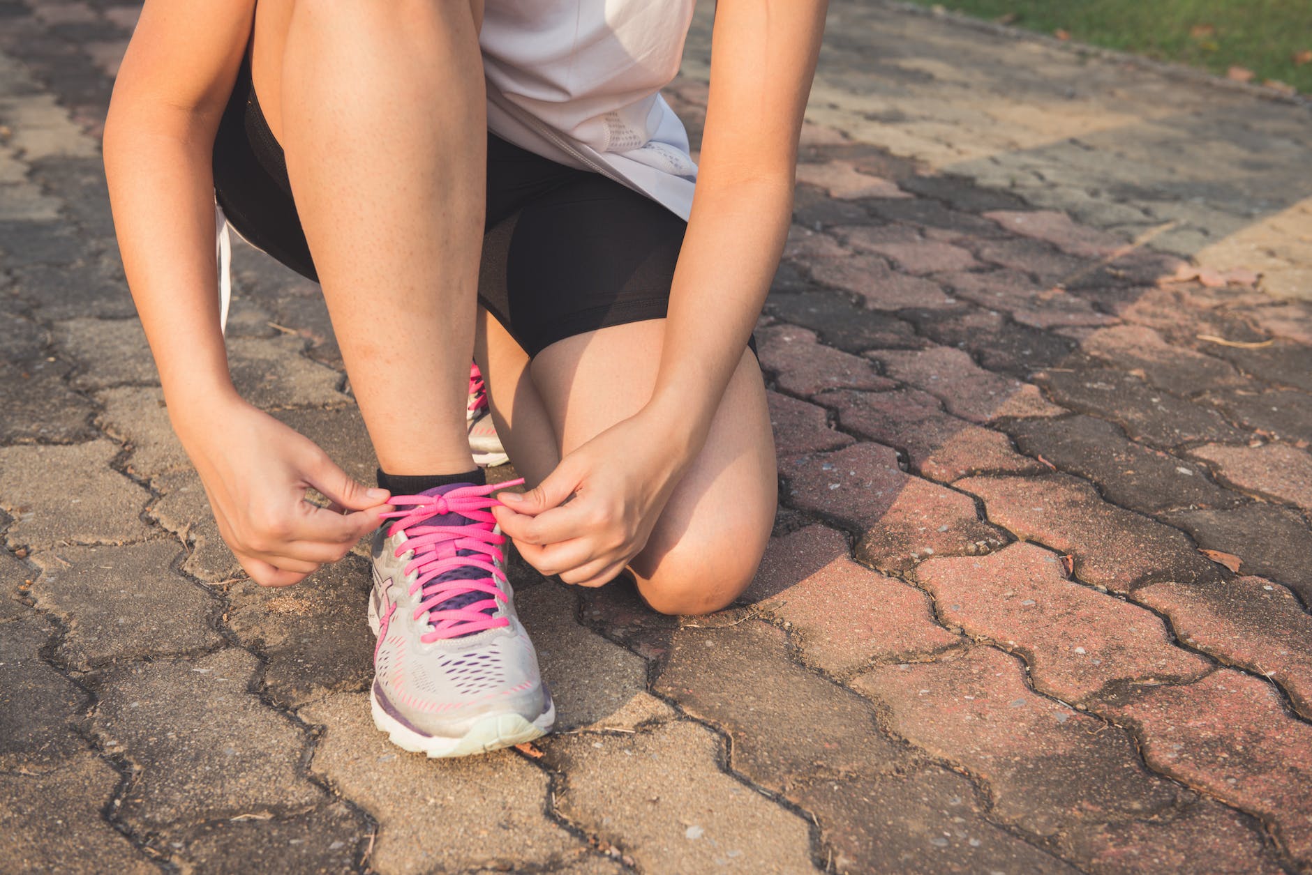 woman lacing up her gray and pink nike low top athletic shoe